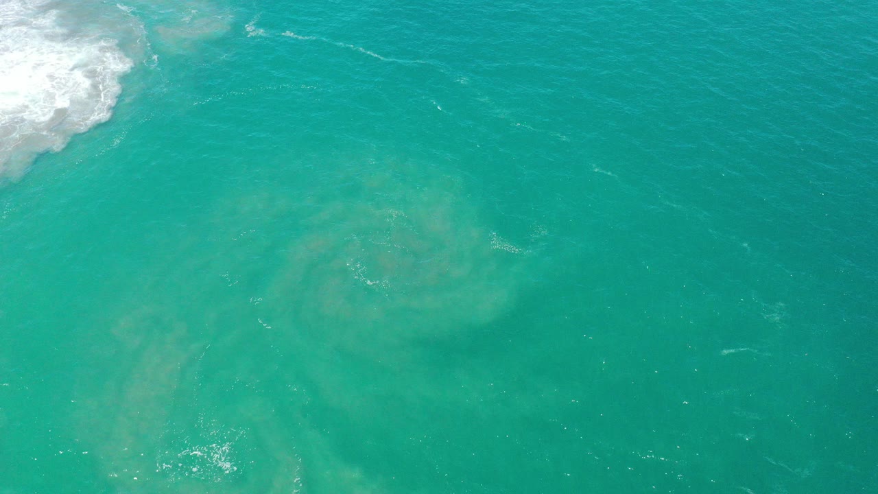 At 0:00, turquoise sea near San Jose Del Cabo fills the frame with pale underwater sediment patterns, white wave foam at the upper left, and no visible people.