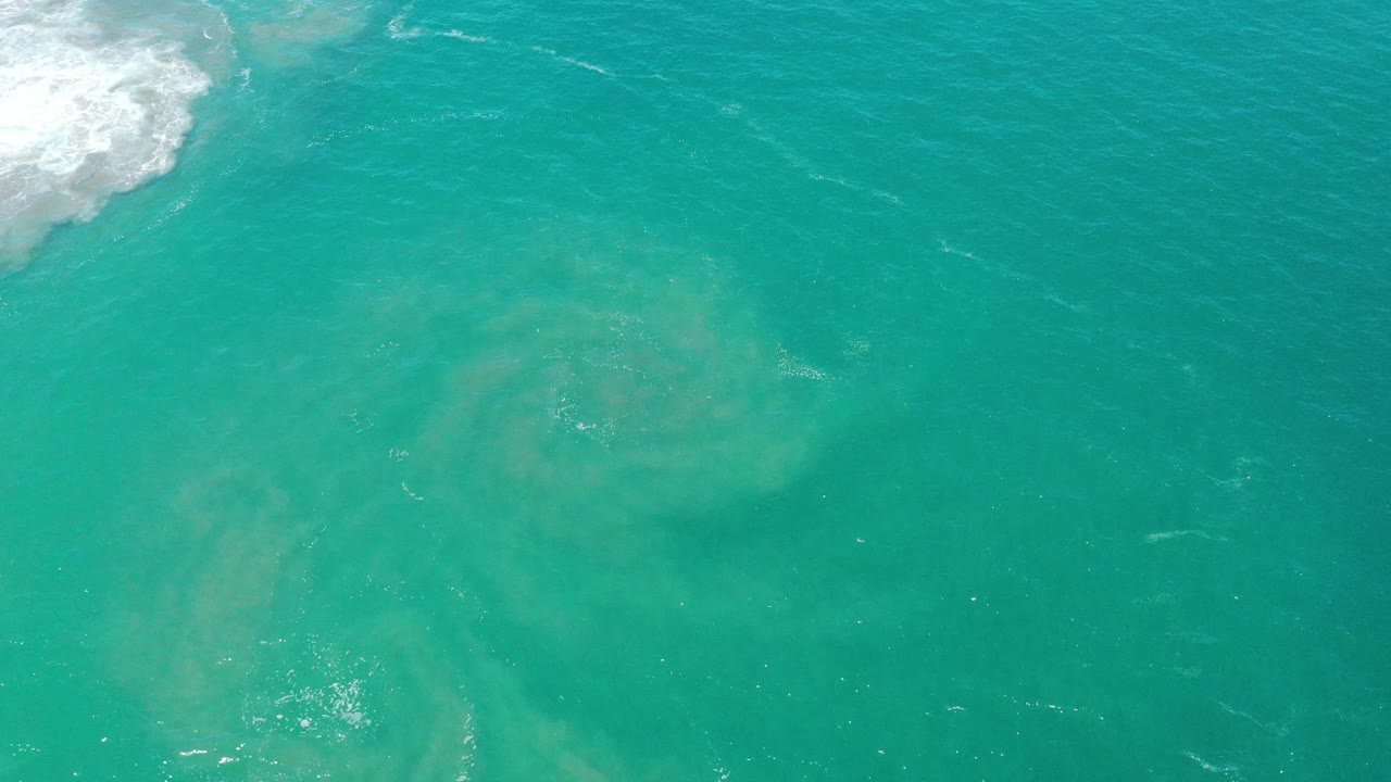 Open turquoise water with diffuse sediment clouds and faint foam traces.