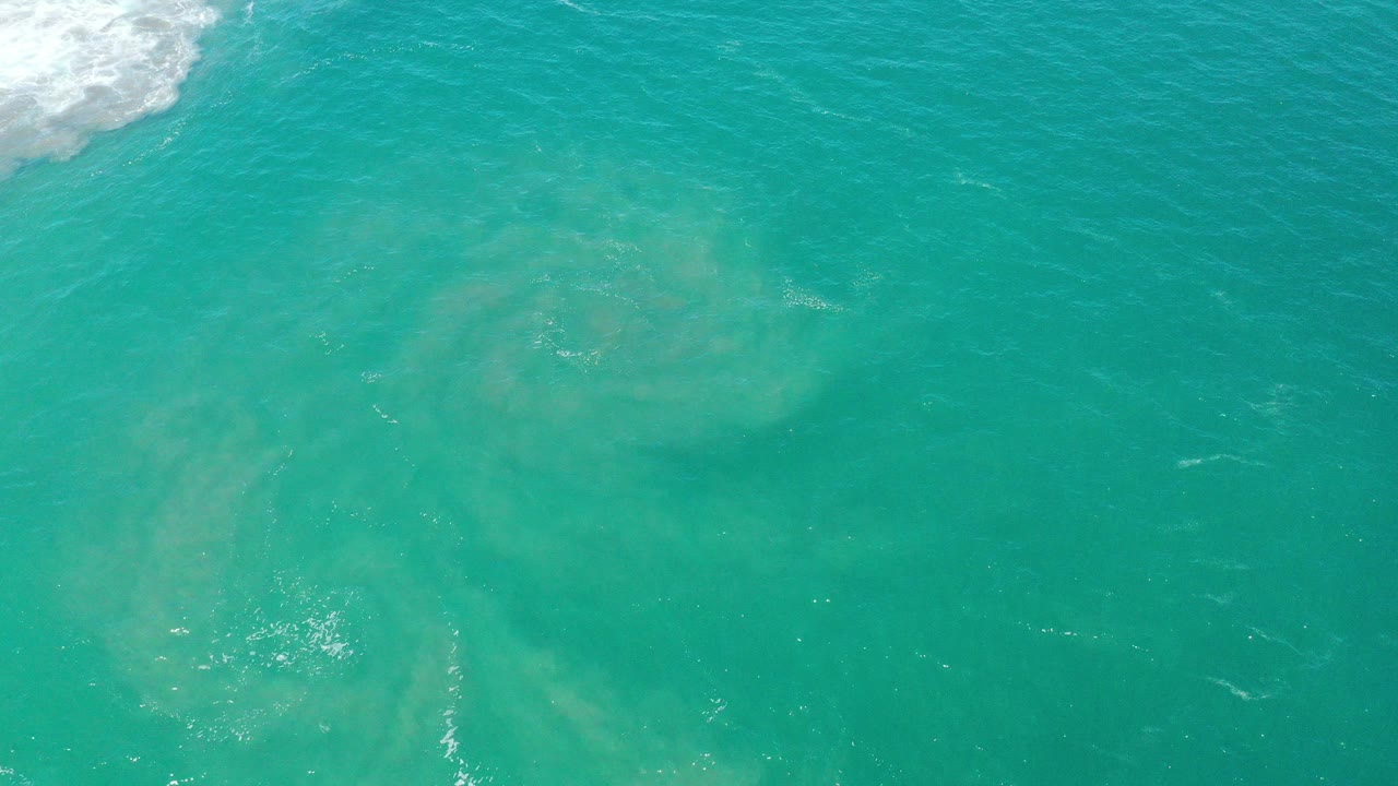 Opening overhead view of turquoise ocean in San Jose del Cabo, Mexico, with pale underwater sand tones, small foam at the upper left, and no visible people.