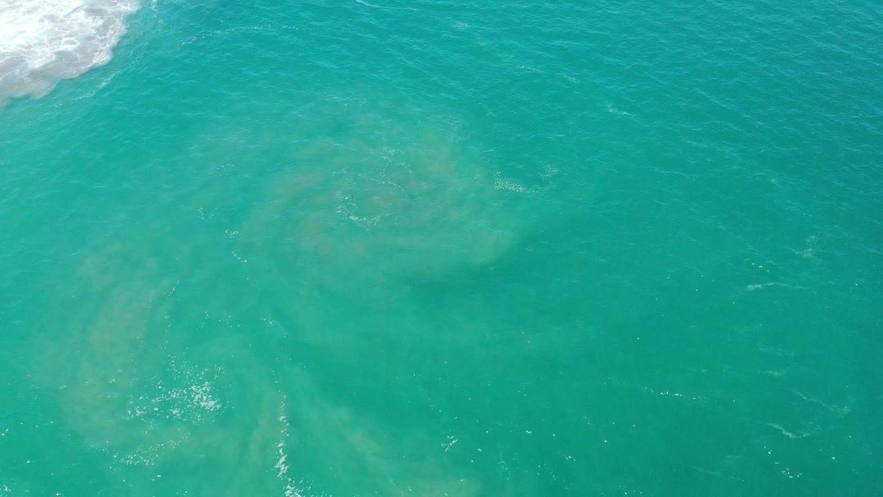 Aerial view of rippled turquoise water with pale submerged sand and faint white streaks.