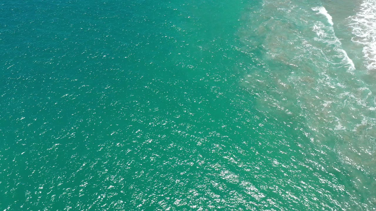 Turquoise ocean surface with white surf angled along the upper right.