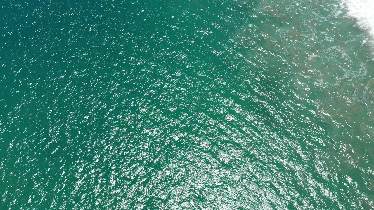 Top-down turquoise-green sea with a narrow band of white surf along the upper right.
