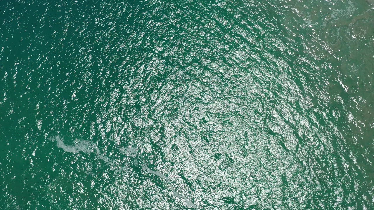 Overhead teal water with bright sun reflections and small ripples.