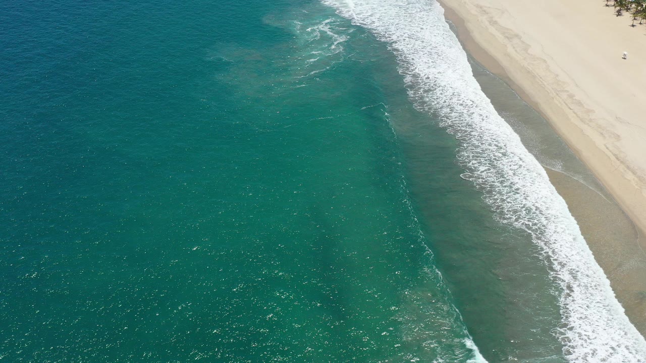 Aerial view of turquoise ocean waves breaking along a sandy beach.