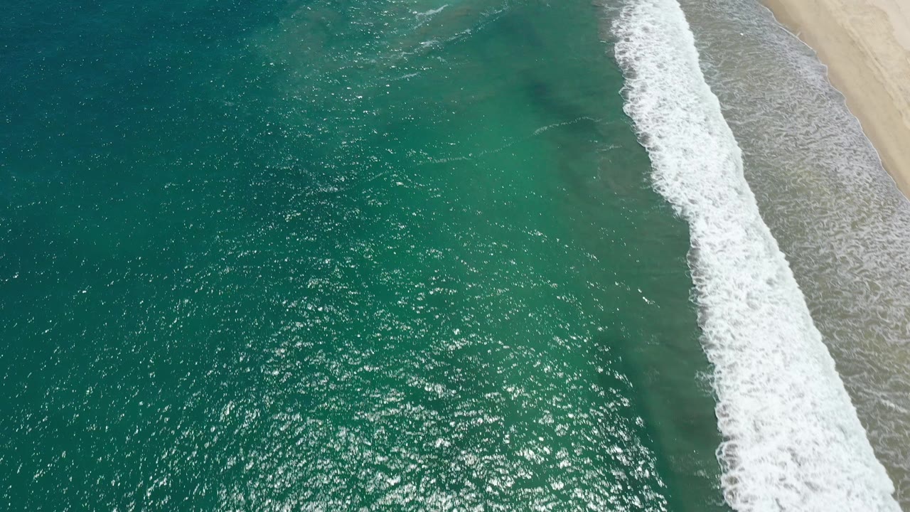 White surf breaks along the right side of clear teal ocean water.