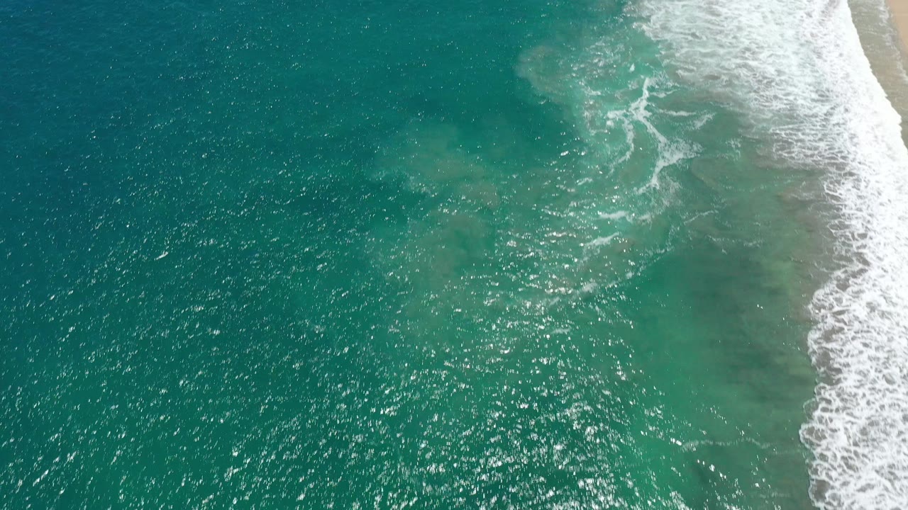 Turquoise ocean surface with surf curling along the right edge.
