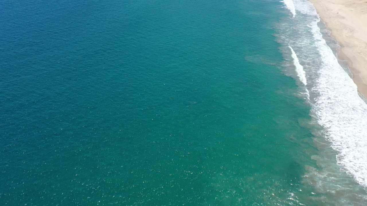 Aerial view of turquoise water meeting a sandy beach with white surf.