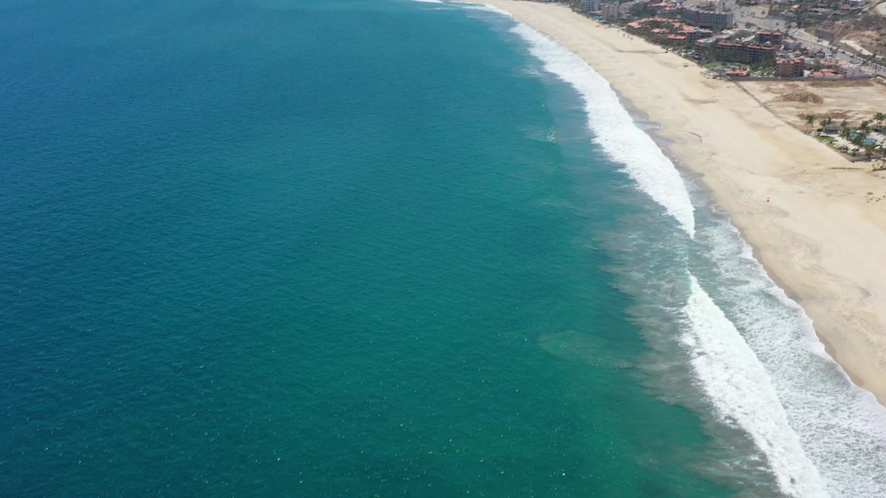 Aerial view of blue ocean beside a sandy beach and surf line.