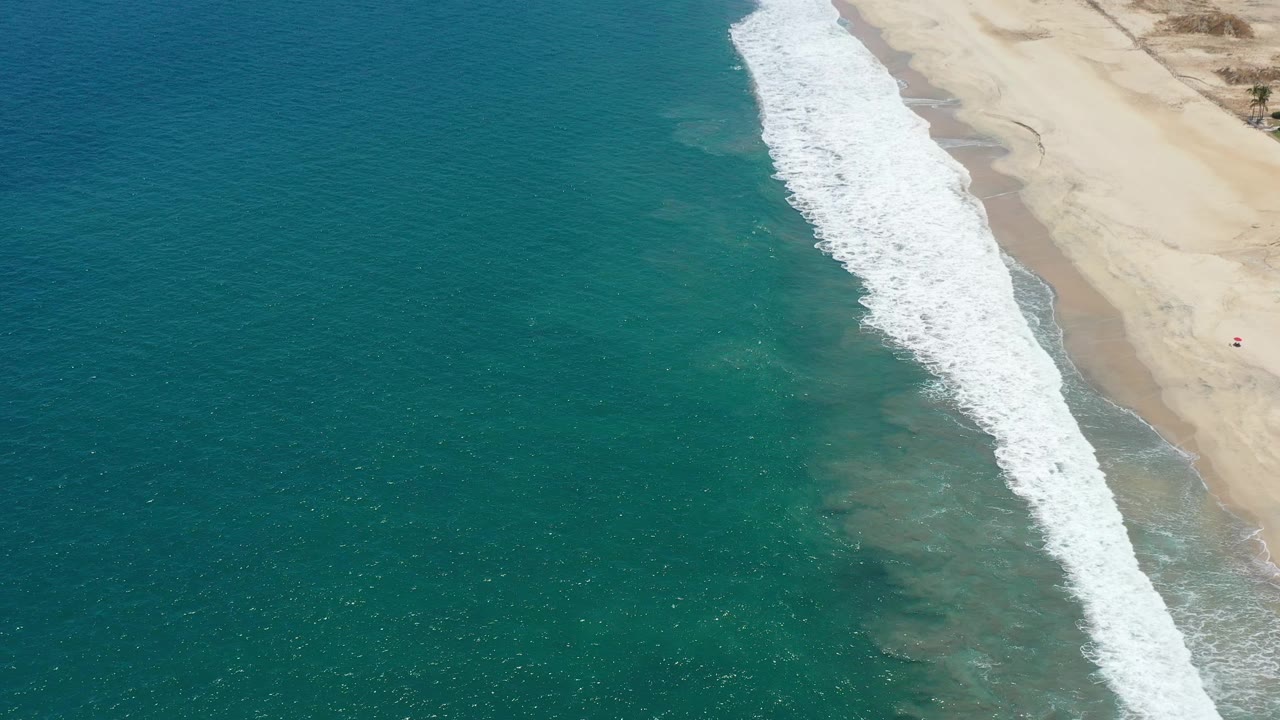 Oblique aerial of surf curling onto a light sand beach.