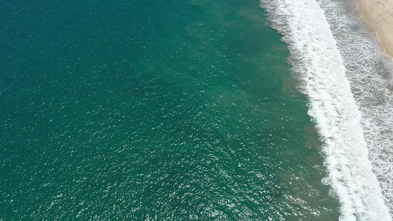 Sparkling green-blue water fills most of the frame with surf at right.