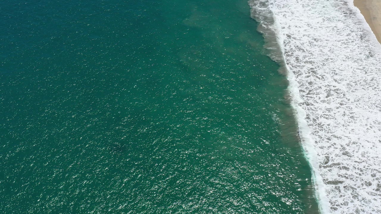 Turquoise ocean and white surf breaking beside a sandy beach