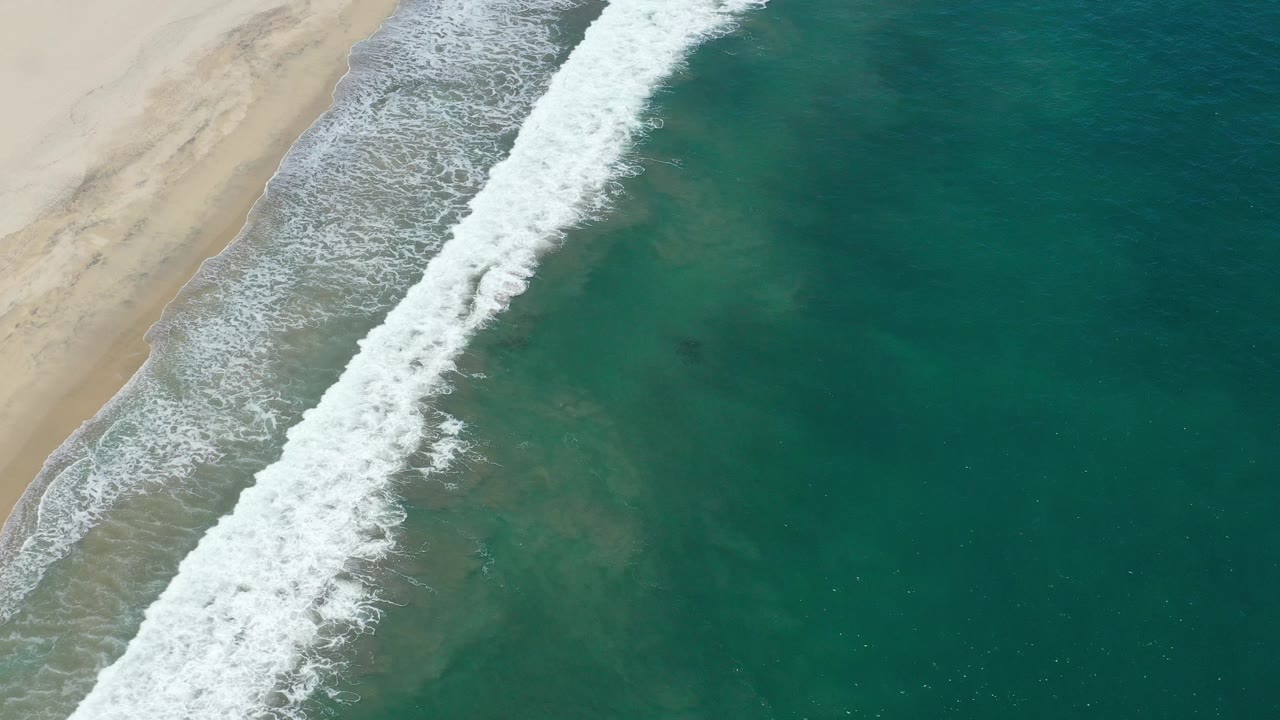 Foamy surf breaks in a thick diagonal band between sand and open water.