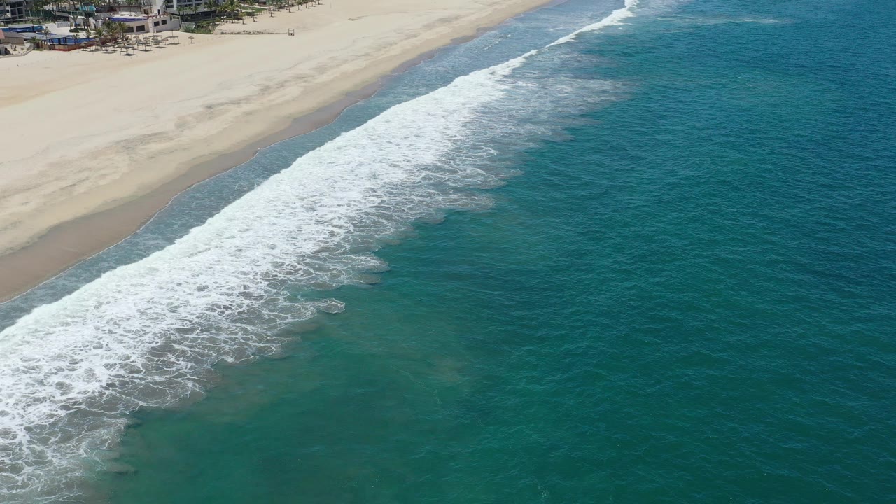 Aerial shoreline view with surf washing across wet sand.