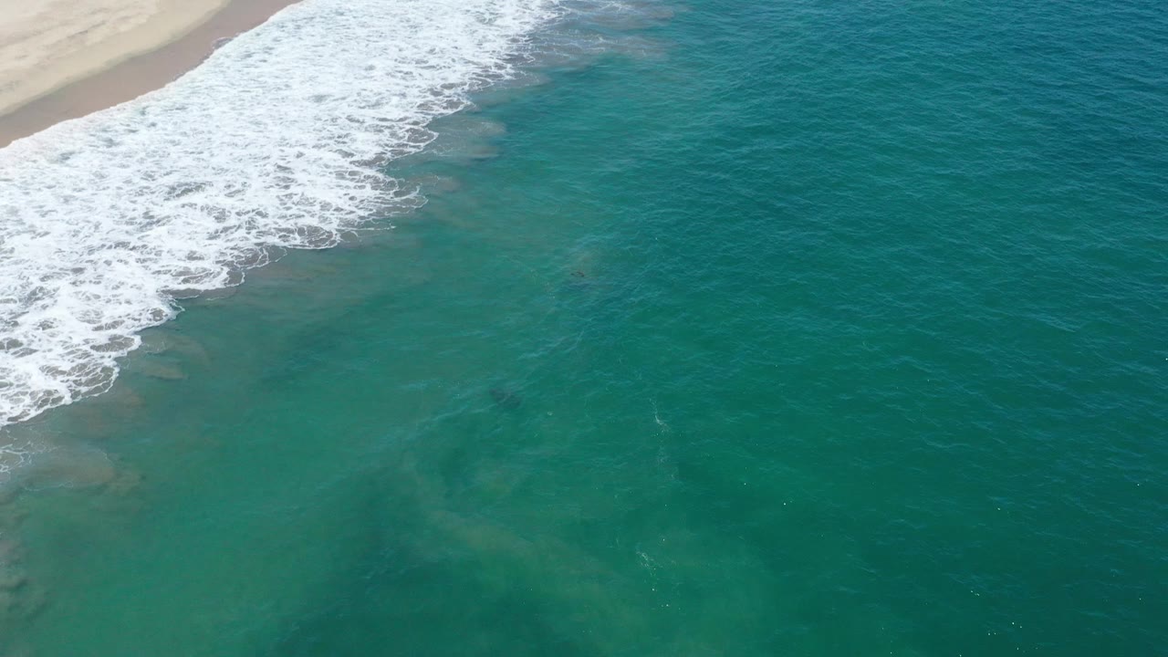 White beach break at the top left with open green-blue ocean below.