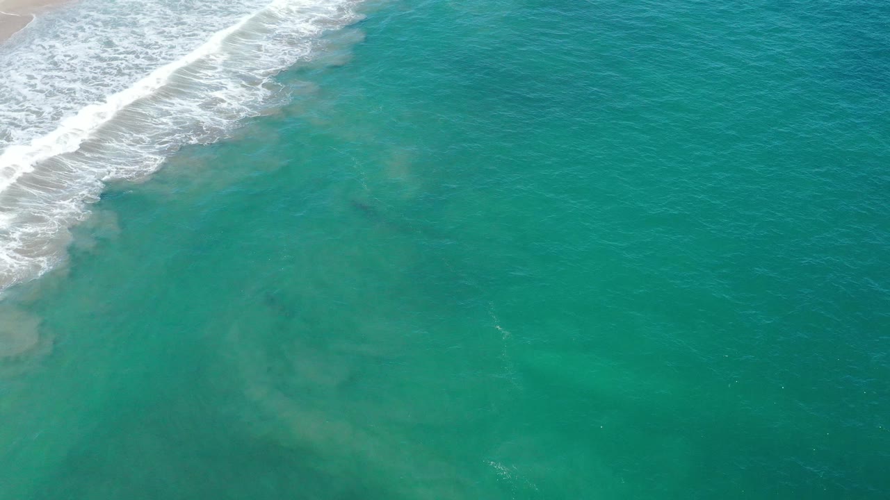 Turquoise sea surface with white surf and cloudy shallows near the top left.