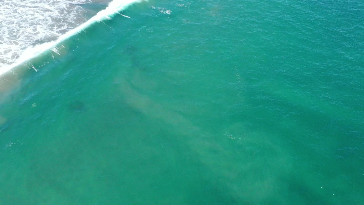 Aerial view of turquoise ocean water in San Jose del Cabo, Mexico, with white surf crossing the upper left corner and no visible people.