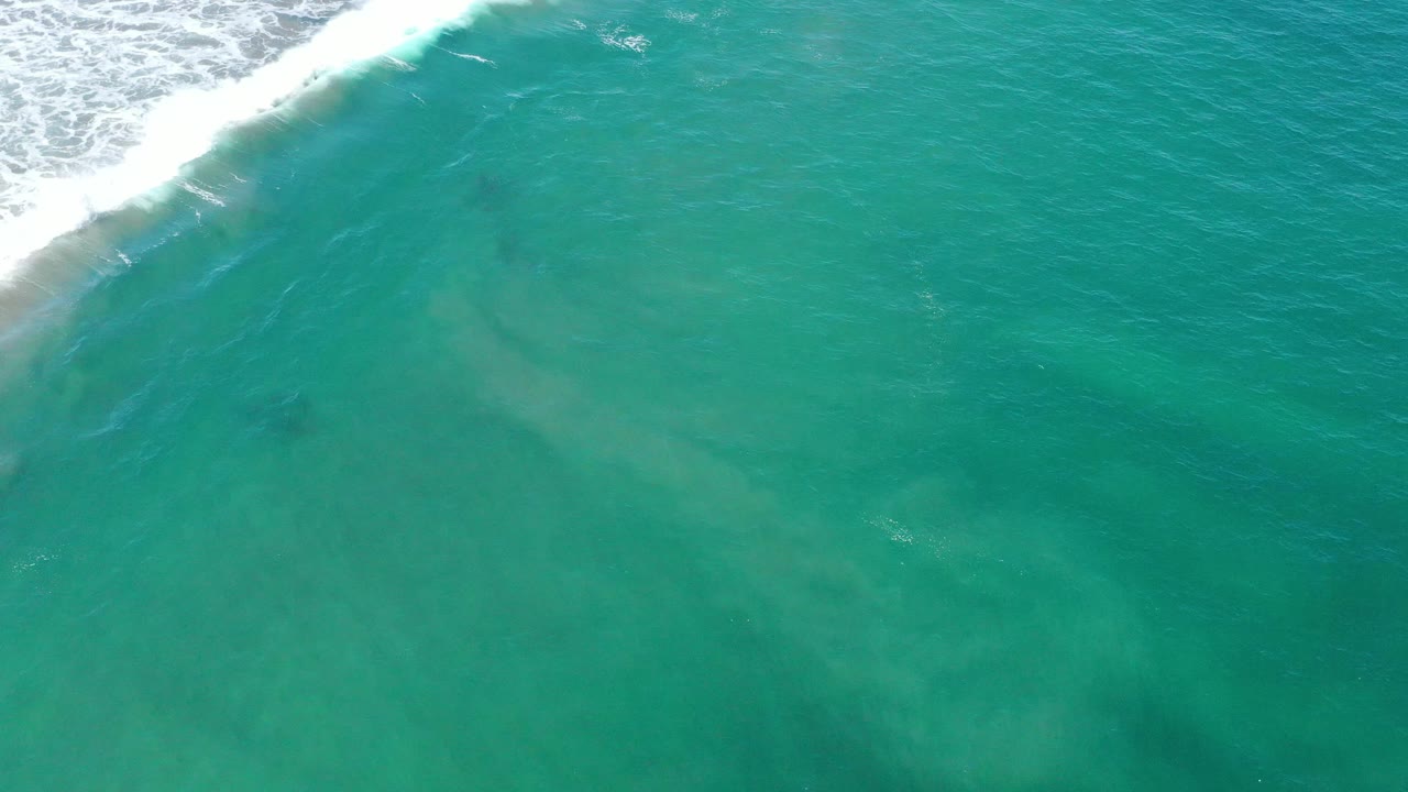 Open turquoise water with a diagonal band of white wave foam at the top left.