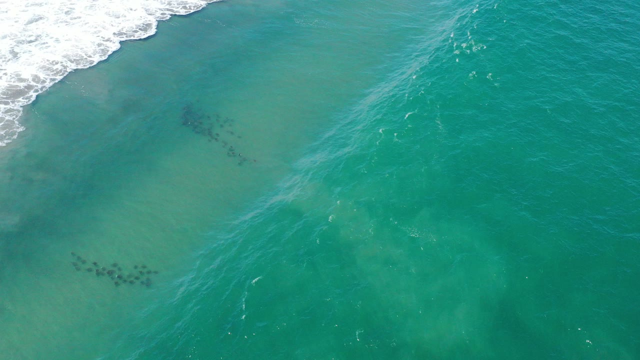 Overhead view of turquoise water in San Jose del Cabo with a faint diagonal wave ripple, darker underwater patches, and no visible people.