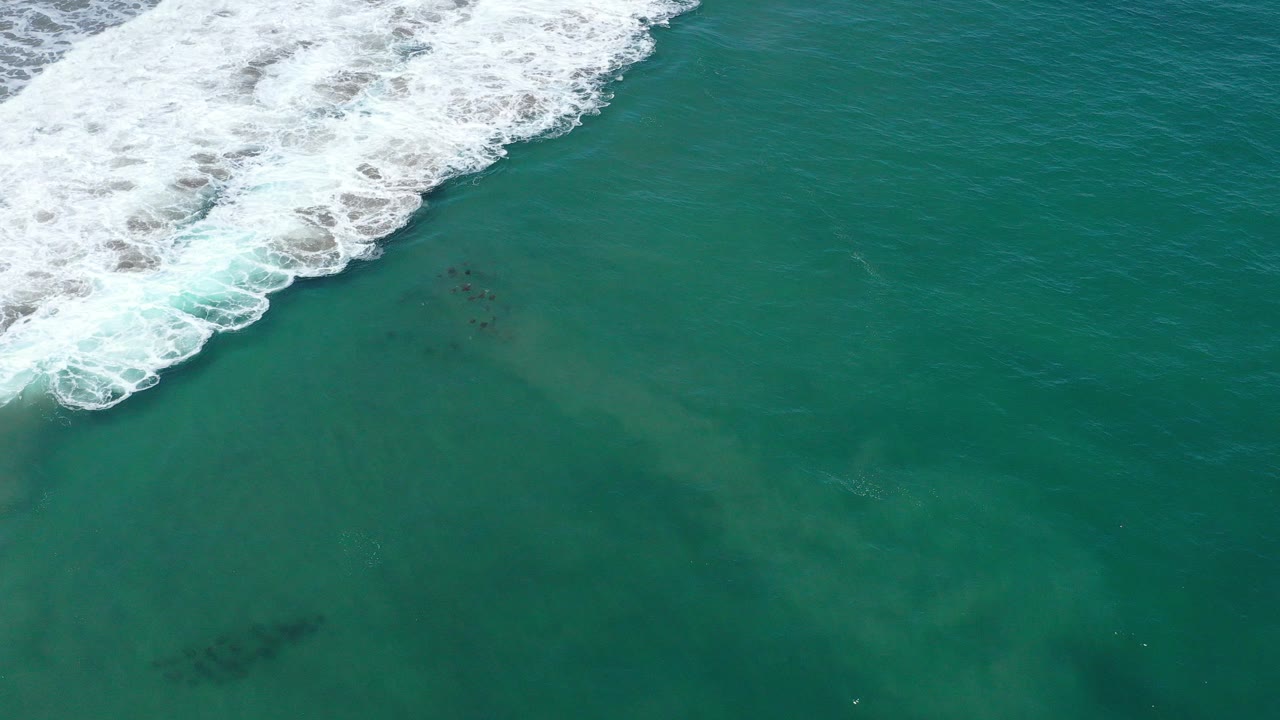 Top-down aerial view of teal ocean near San Jose del Cabo, Mexico, with foamy white surf along the upper left and no visible people.