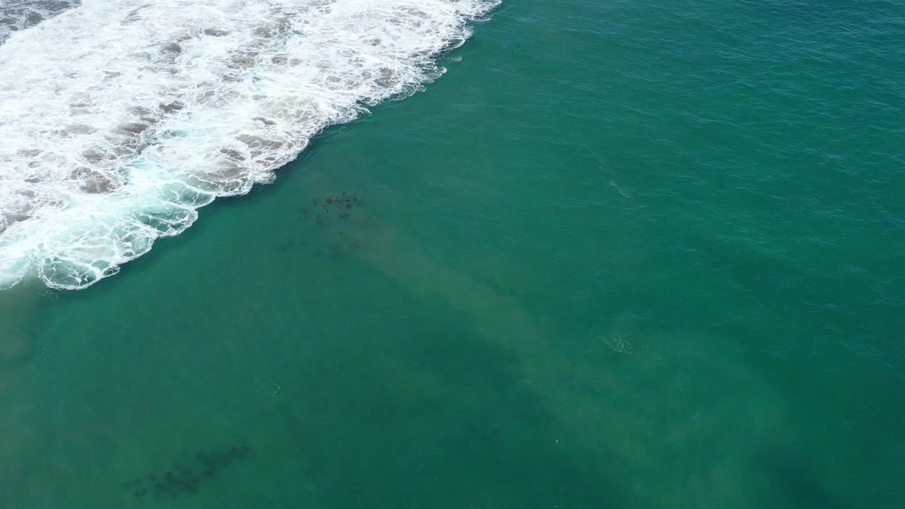 Overhead San Jose del Cabo ocean view with a diagonal band of breaking surf near the top and darker underwater shapes below, with no visible people.