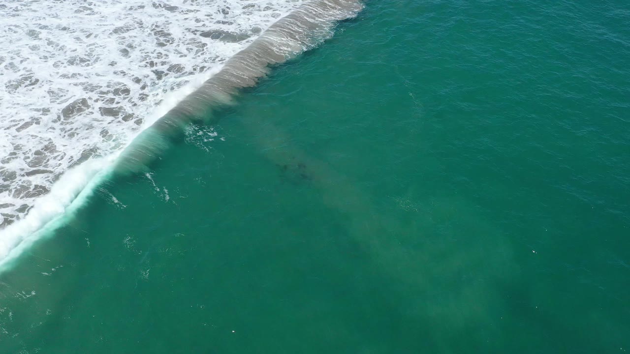 Aerial frame of San Jose del Cabo green water, with the white wave band still near the upper left and soft underwater clouding visible below, no visible people.