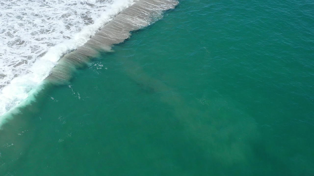 Top-down view of turquoise green sea in San Jose del Cabo, Mexico, with breaking white surf pressed into the upper left corner and no visible people.
