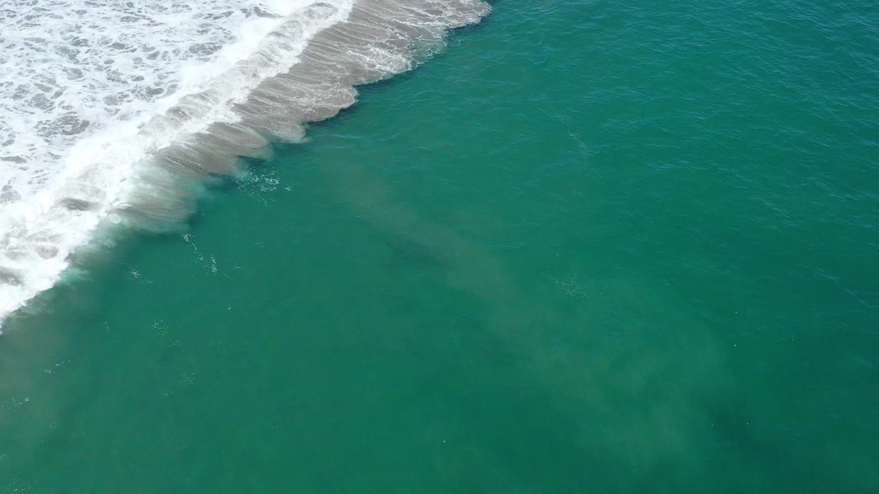 White shoreline foam crosses diagonally over green sea water.