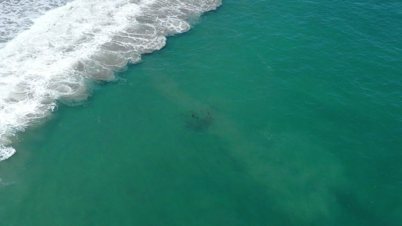 Overhead view of green ocean water in San Jose del Cabo, Mexico, with white foamy surf entering from the upper left and no visible people.