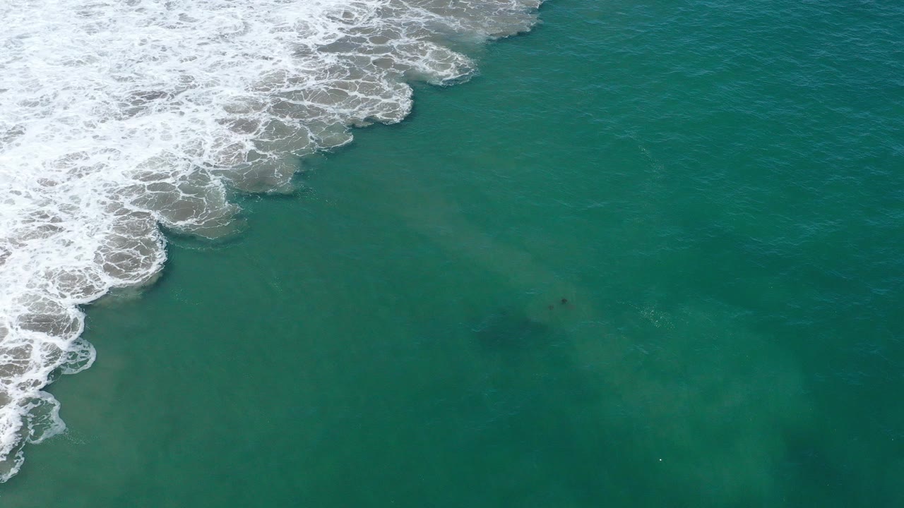 Overhead view of teal ocean in San Jose del Cabo, Mexico, with white surf spreading from the upper left and no visible people.