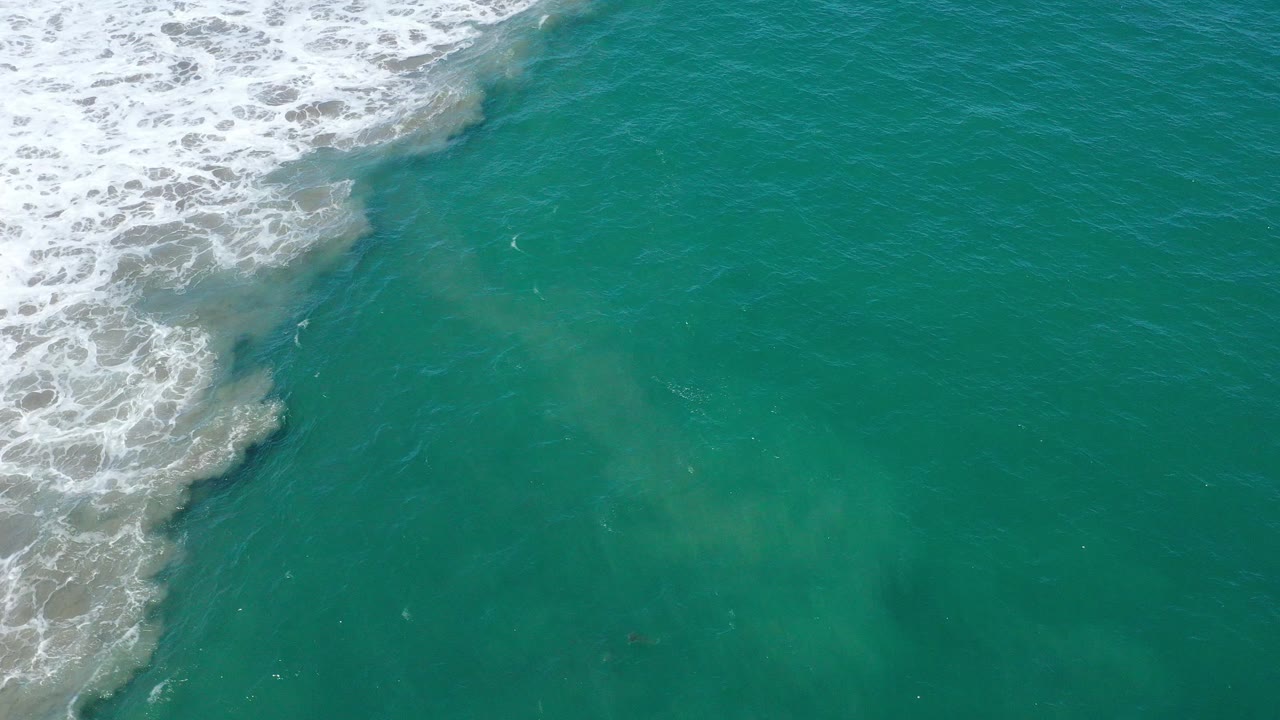 Top-down view of teal water in San Jose del Cabo with white surf along the upper left edge and no visible people.