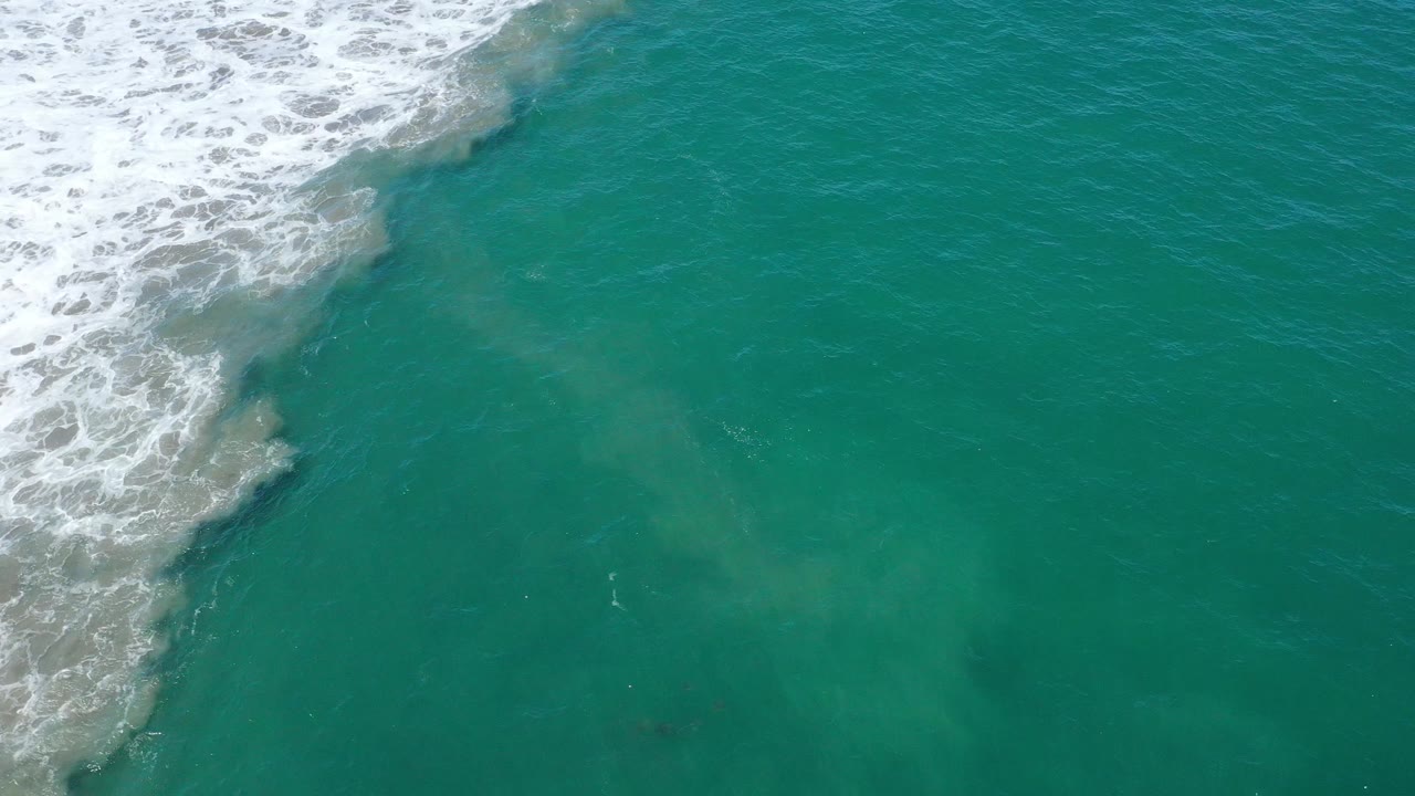 White surf curves into teal water from the upper left.