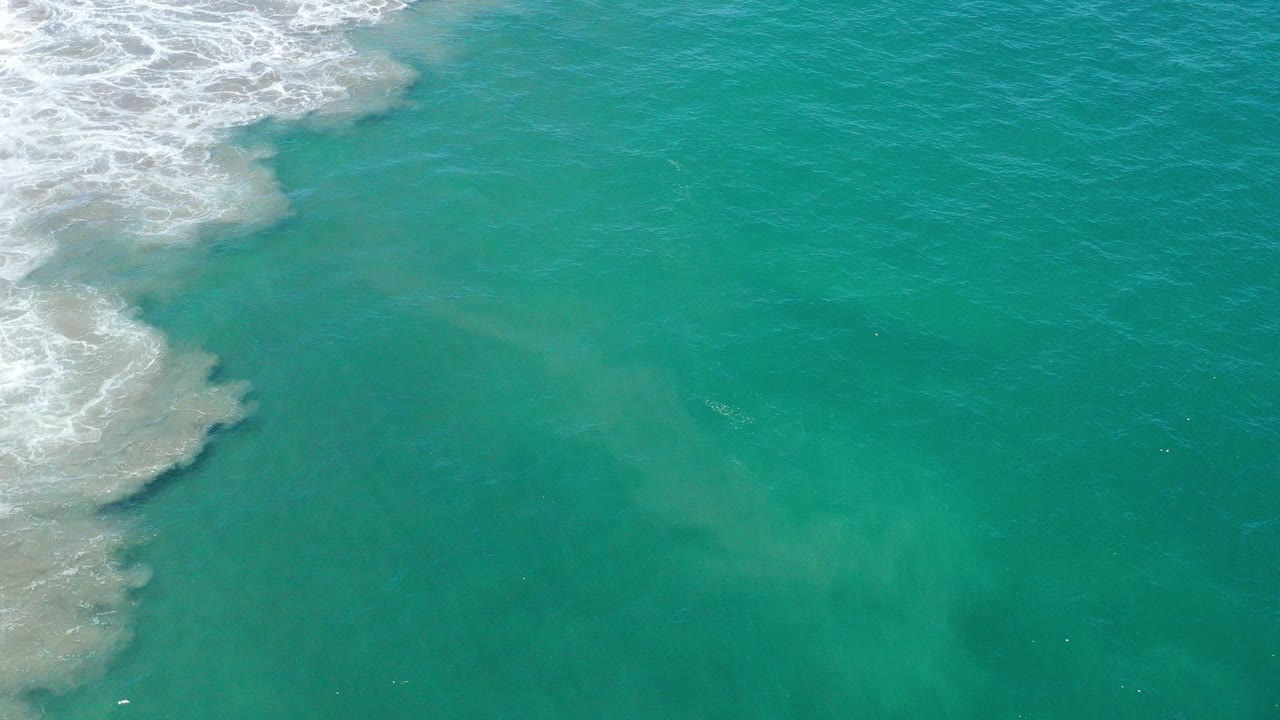 Turquoise ocean water with white foam entering from the upper left.