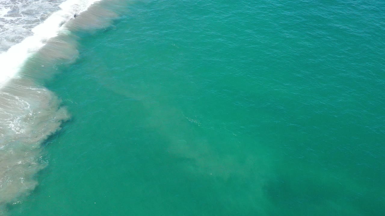 Overhead view of turquoise ocean near San Jose del Cabo, Mexico, with white surf breaking along the upper left edge and no visible people.