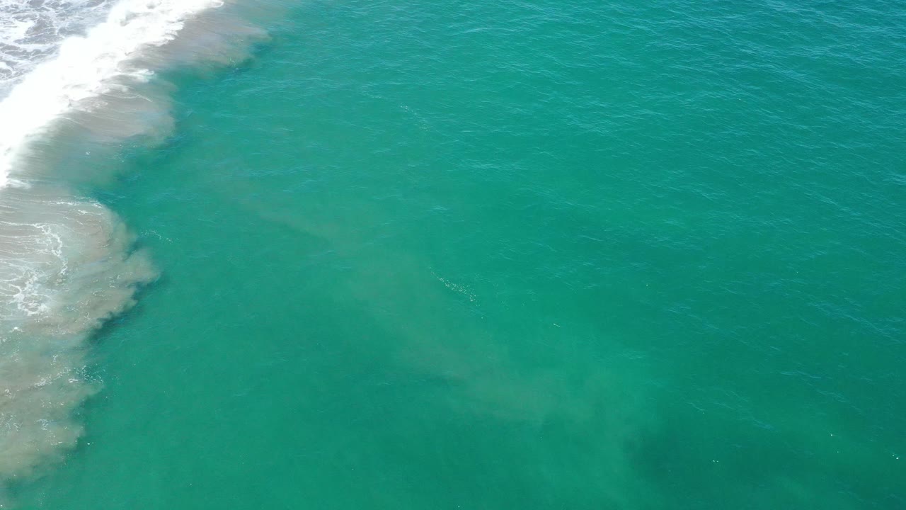 Top-down ocean surface with breaking surf at the upper left and darker water patches.