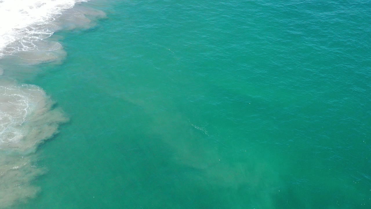 Teal ocean water with white surf foam along the upper left edge.