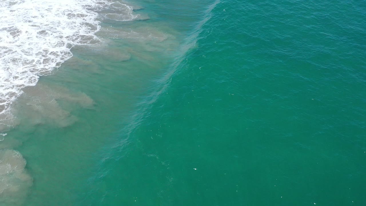 A faint diagonal wave line crosses teal water beside foamy surf.