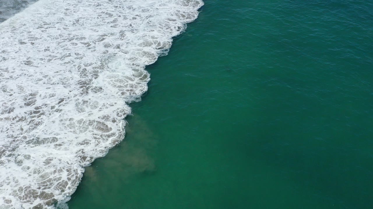 Aerial view of white surf over teal ocean water