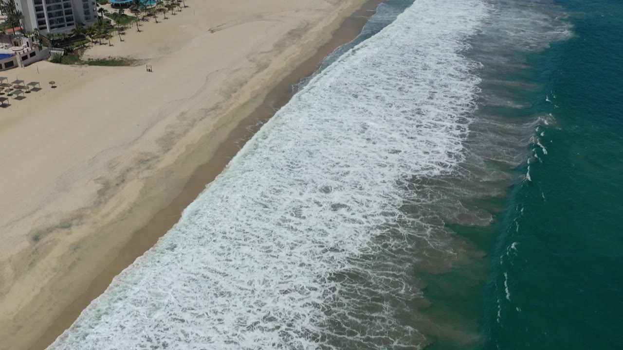 Aerial coastline with resort buildings at the top and waves below.