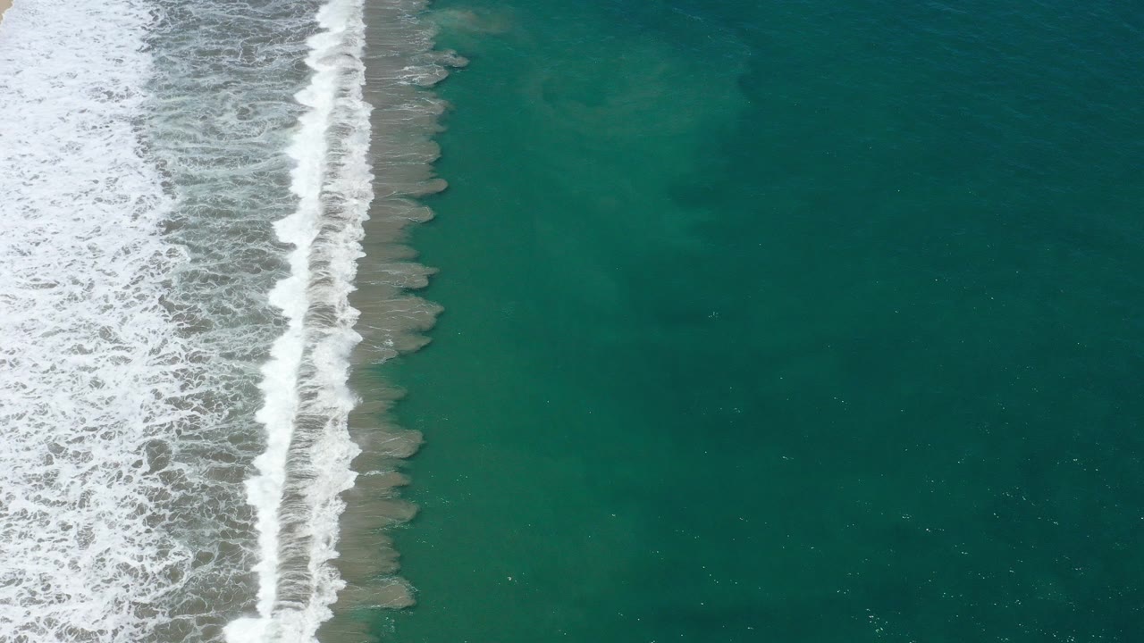 Overhead view of white surf running down the left side of San Jose del Cabo water, with teal ocean filling the right side and no visible people.