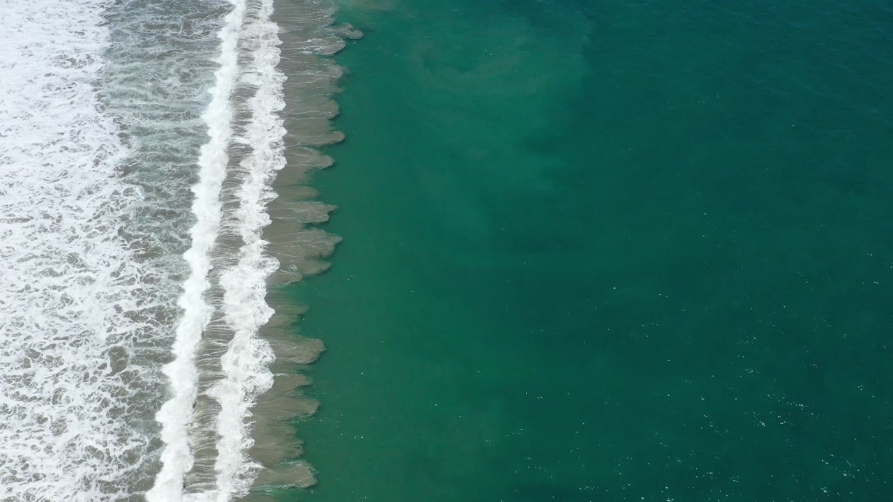 Aerial view of surf foam and open teal sea.