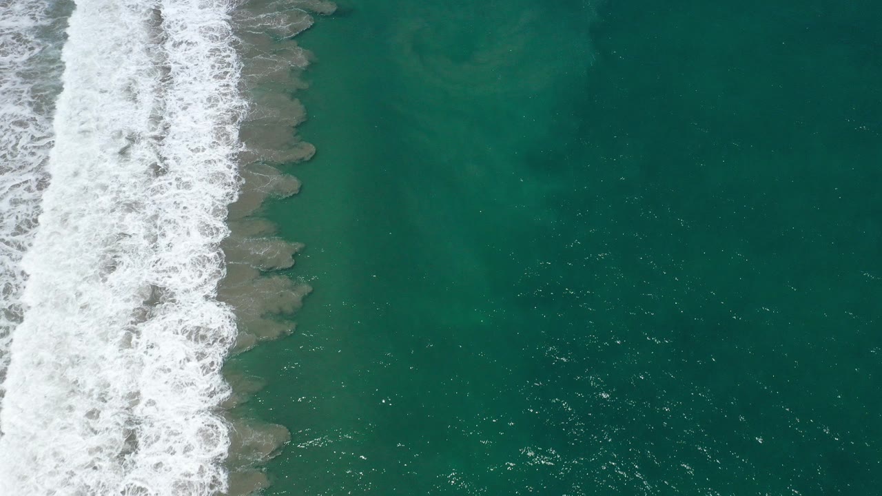 Overhead view of white surf foam running down the left side of teal water in San Jose del Cabo, Mexico, with no visible people.