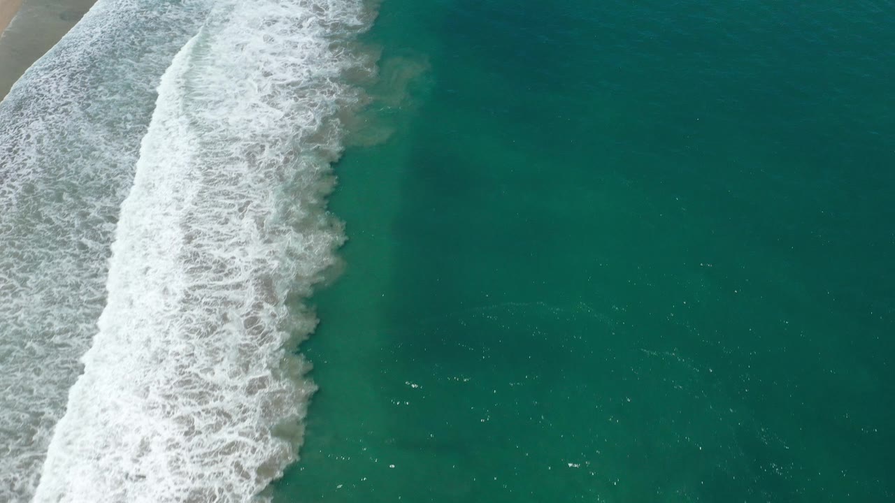Diagonal surf line beside darker teal ocean water.
