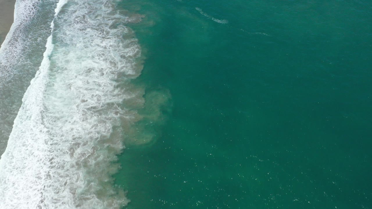 Overhead view of turquoise water in San Jose Del Cabo, Mexico, with a thick white surf line pushing in from the left and no visible people.