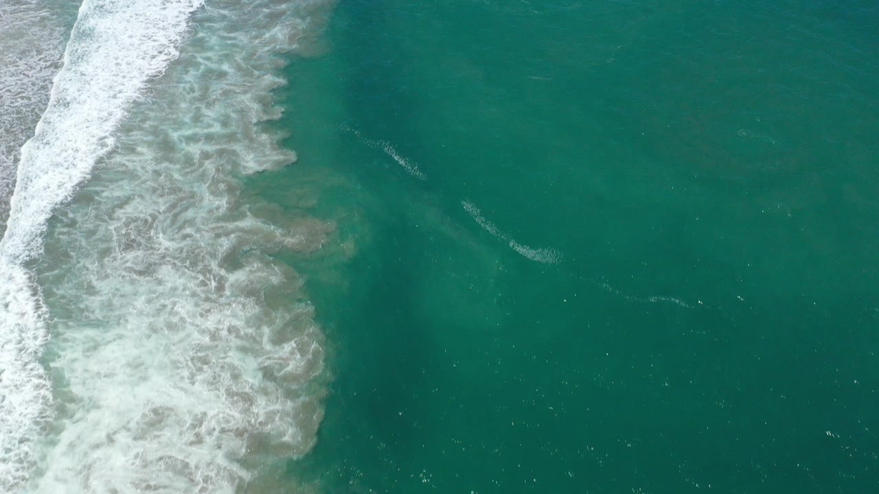 Top-down frame of deep green water and white surf rolling along the left side in San Jose Del Cabo, Mexico, with no visible people.