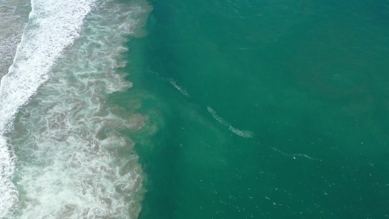 Foamy surf borders deep green water from above.
