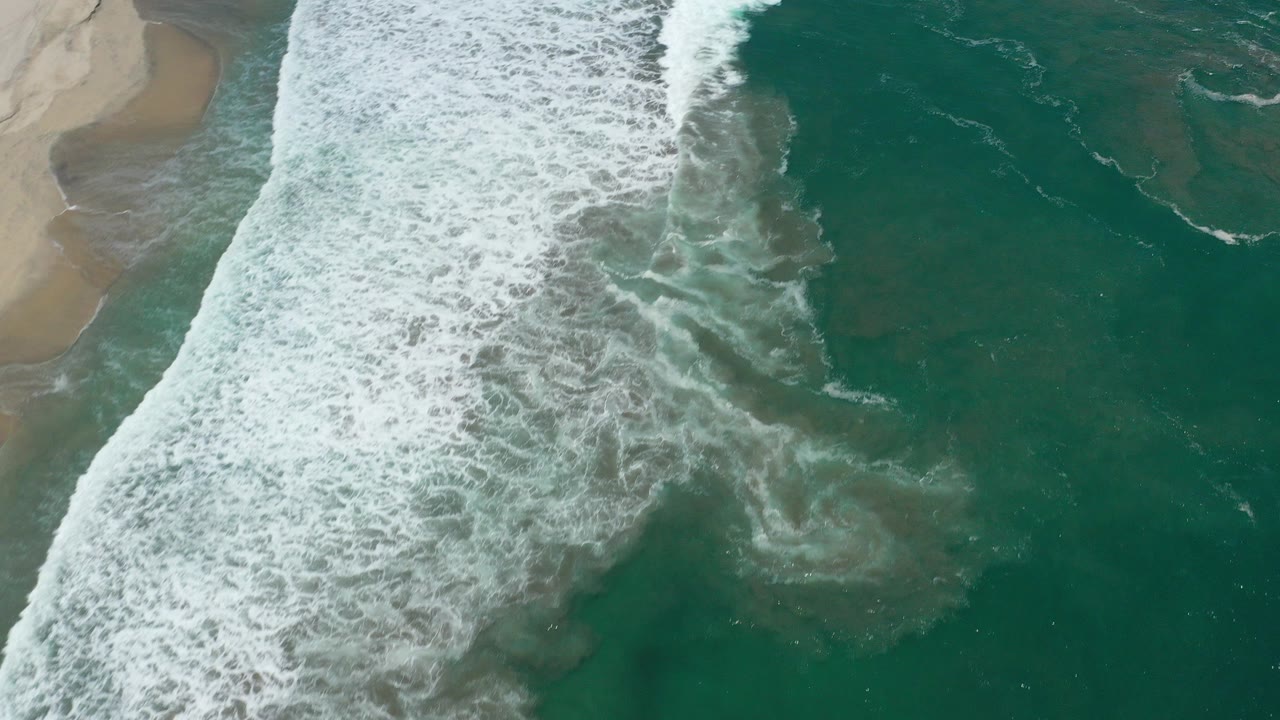 Overhead surf breaking beside teal ocean and sand