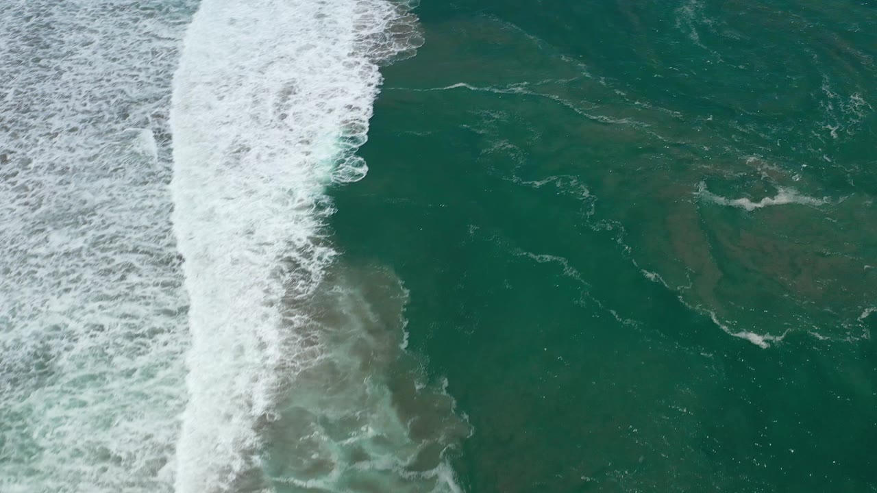 Aerial frame over San Jose Del Cabo water, where dense white foam borders darker green ocean with no visible people or vessels.
