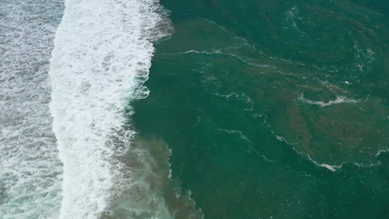 White wave break runs vertically through blue-green ocean water.