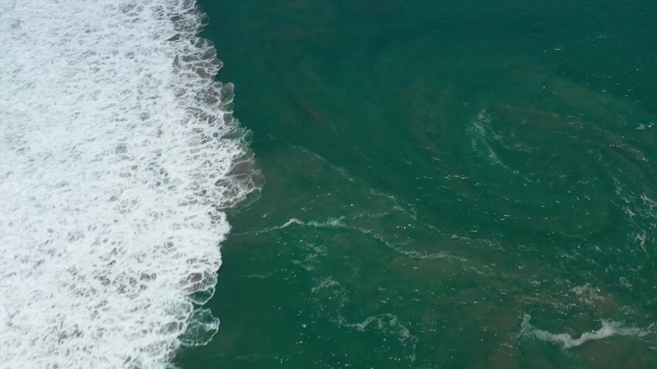 Aerial frame over San Jose del Cabo water, with a dense white breaker cutting through deep teal ocean and no visible people.