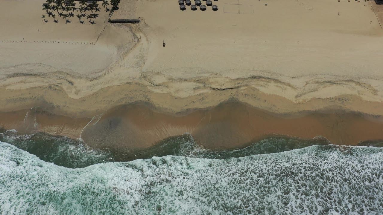 Overhead view of waves breaking onto a sandy resort beach.